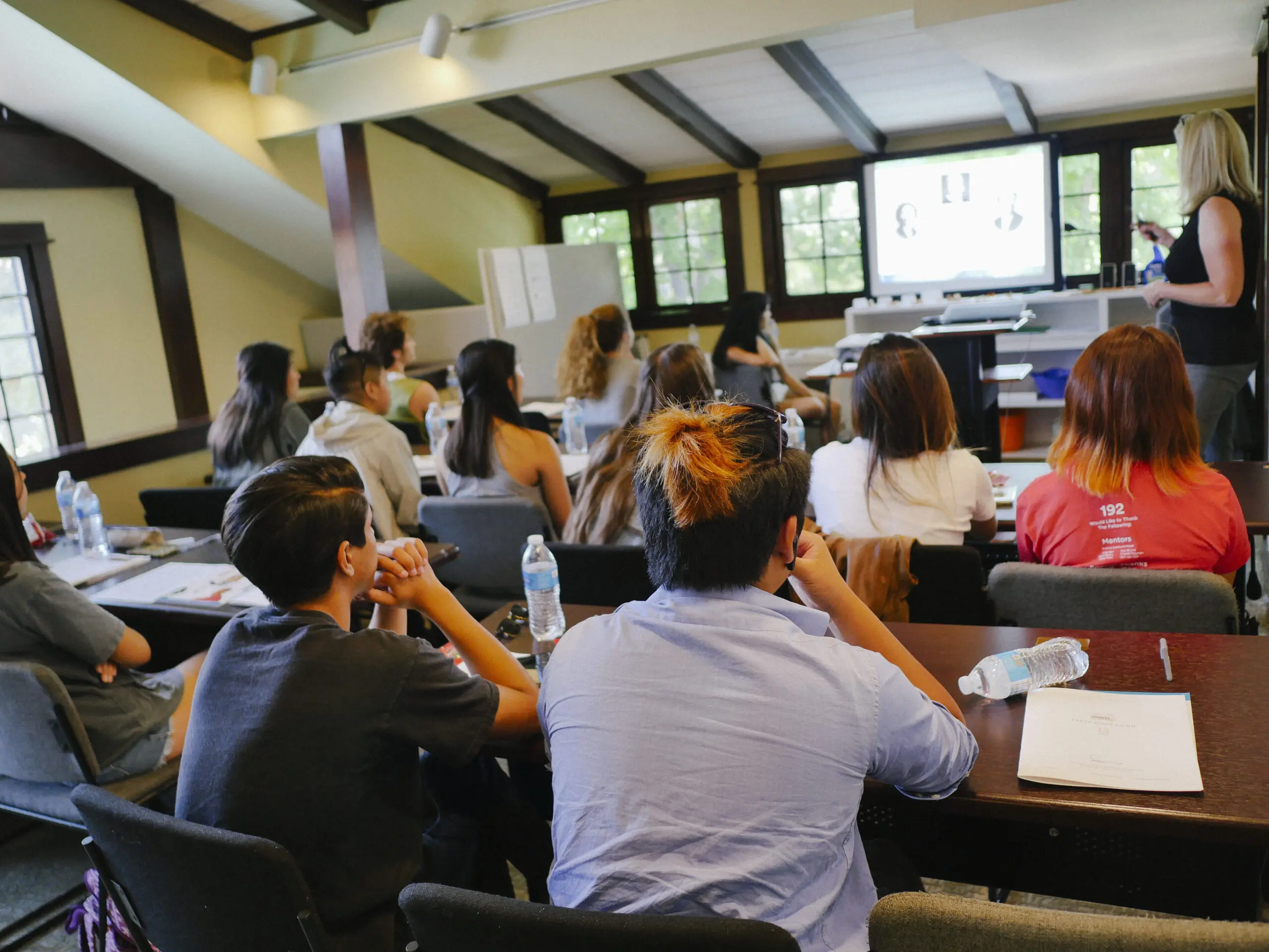 High school students sitting at desks listening to their instructor in front of a monitor